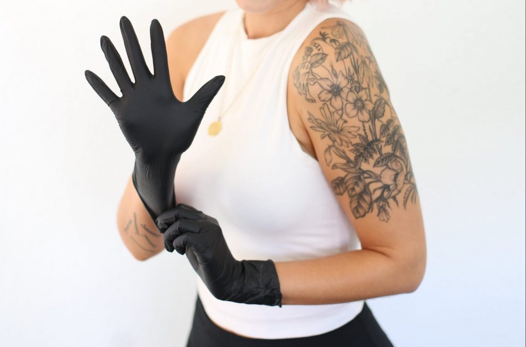 a tattooed lady in a white vest putting on black gloves