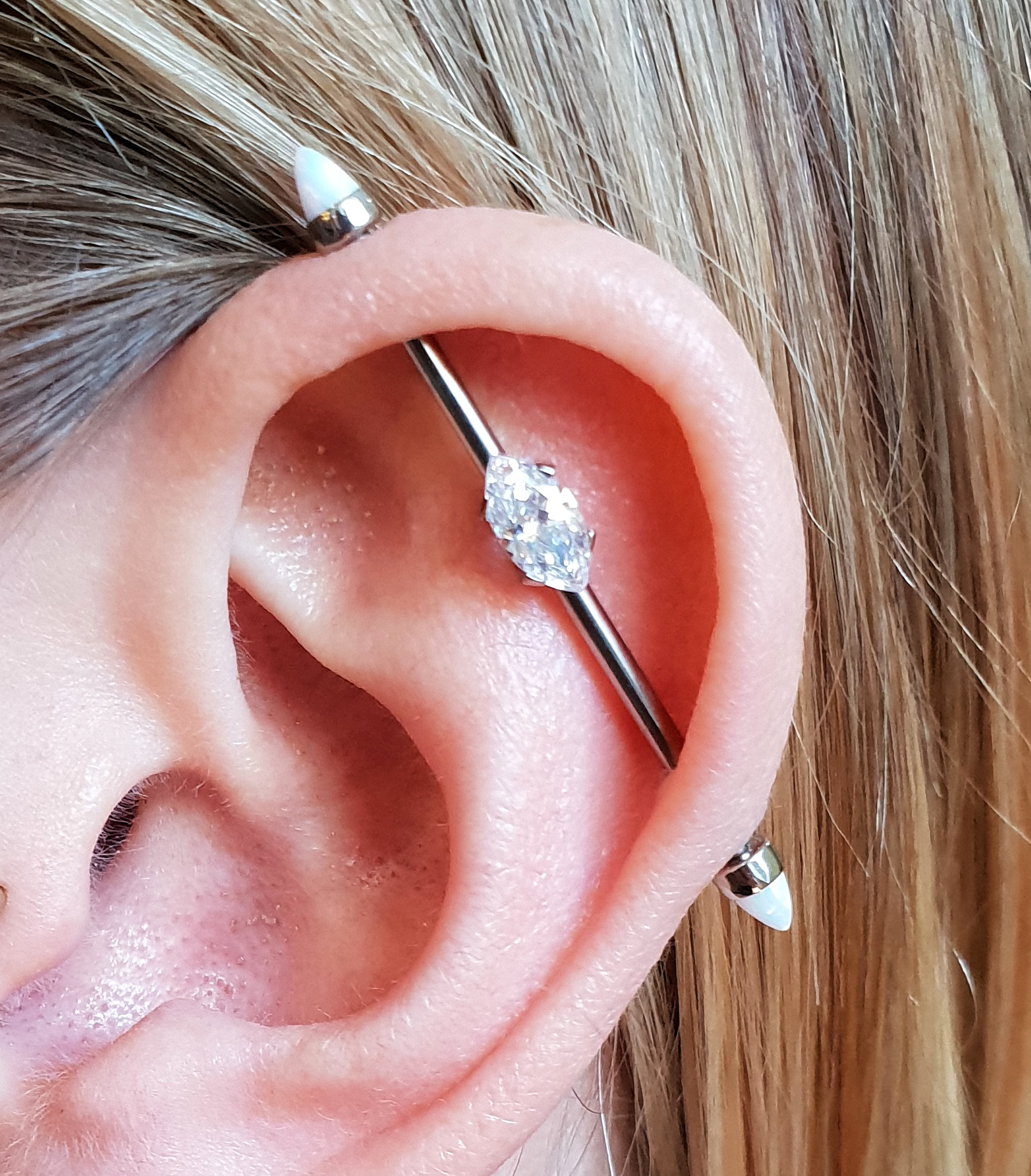 an industrial piercing in titanium with a marquise horizontal cz gem from Anatometal, either end is a white opal cone from the same company