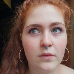 A redheaded girl with big hoop earrings and a turquoise bezel in a captive ring being worn in a septum piercing