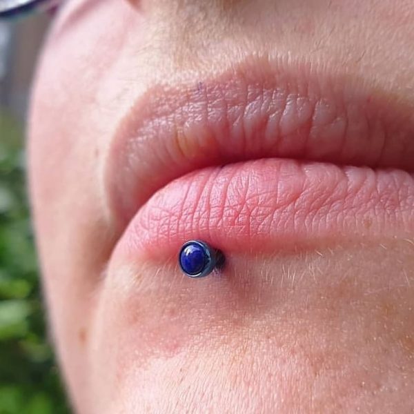 a lip piercing up close with anodized blue jewellery