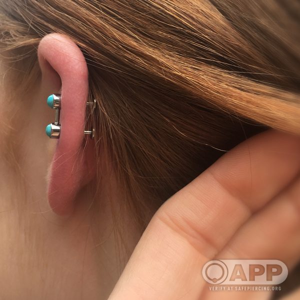 A custom piece of jewellery from Anatometal with two turquoise bezels welded together with a small post between them making the shape of two circles joined with a line. the person needed two piercings for this piece