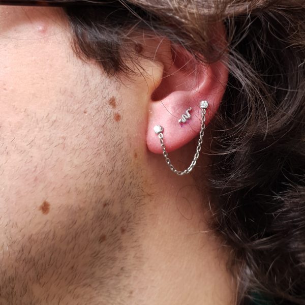 two lobe piercings with a hanging chain from one to the other have a snake end in white gold from Bodygems between them