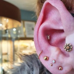 an ear up close, jewellery cabinets are in the background. there are many earlobe piercings with the clients own jewellery but the showcase is the baguette in the conch piercing from Anatometal