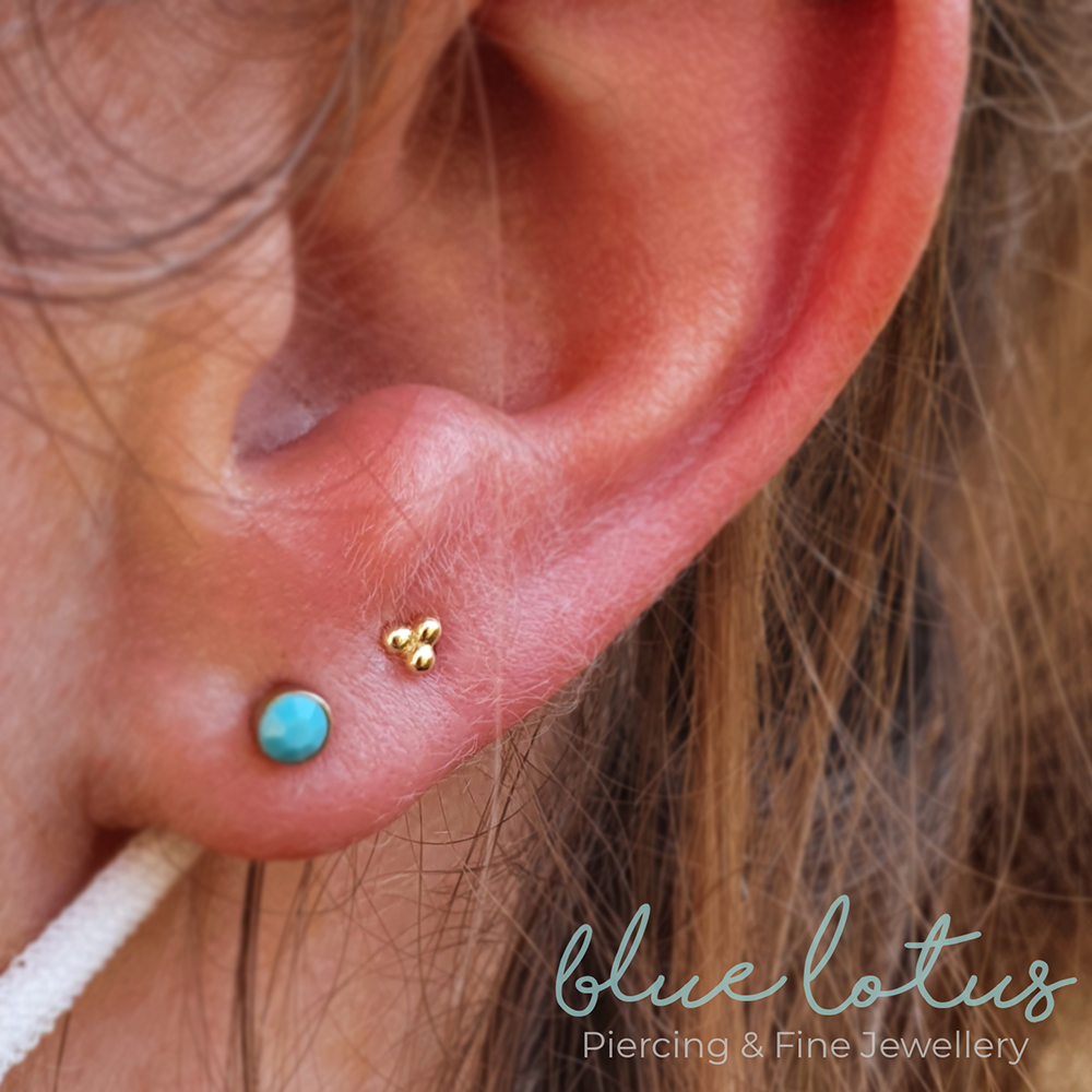 A left ear, first lobe piercing has a blue opal and the second a Tribead in gold from Anatometal