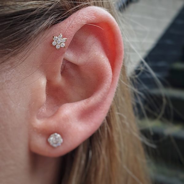 A close up of an ear wearing an 18k solid gold flower in the forward helix from Anatometal and the clients own gem in their lobe
