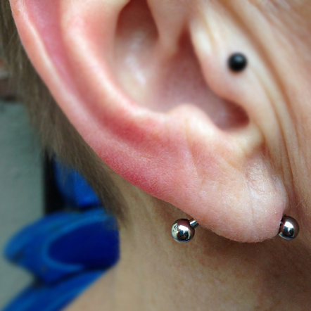 A high polished titanium curved barbell in a horizontal lobe piercing, the person also has a black ball in the tragus