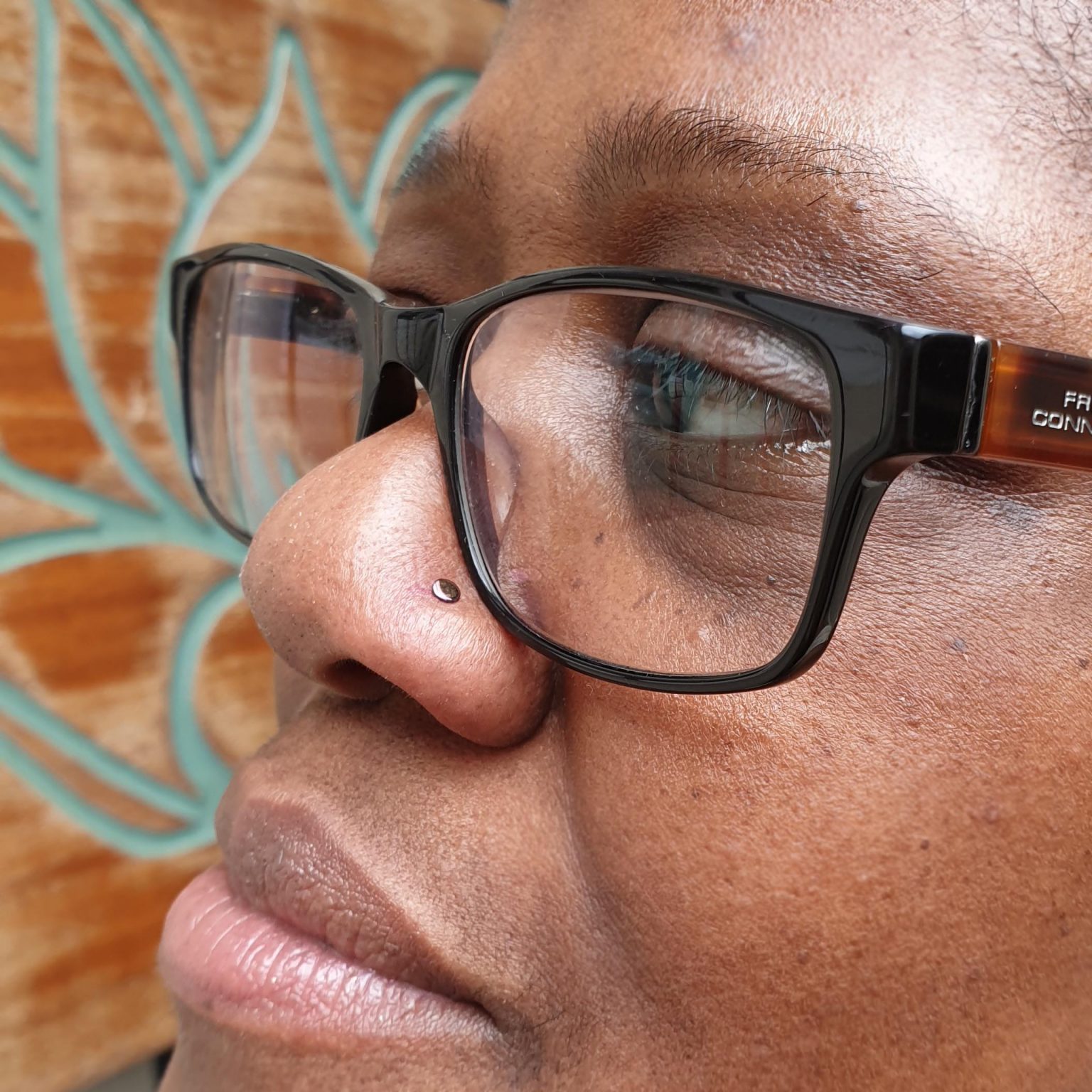 a flat disk on a nose piercing, the lady is wearing black glasses