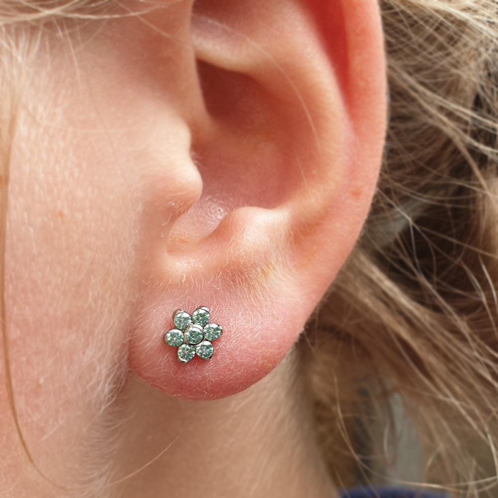 An Anatometal flower with blue gems in a lobe piercing
