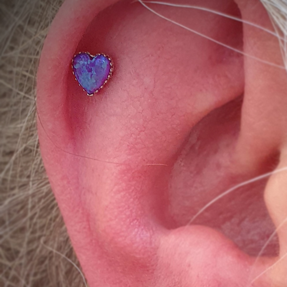 a close up of an ear with an Anatometal Opal heart in the middle of the flat area, the opal is purple