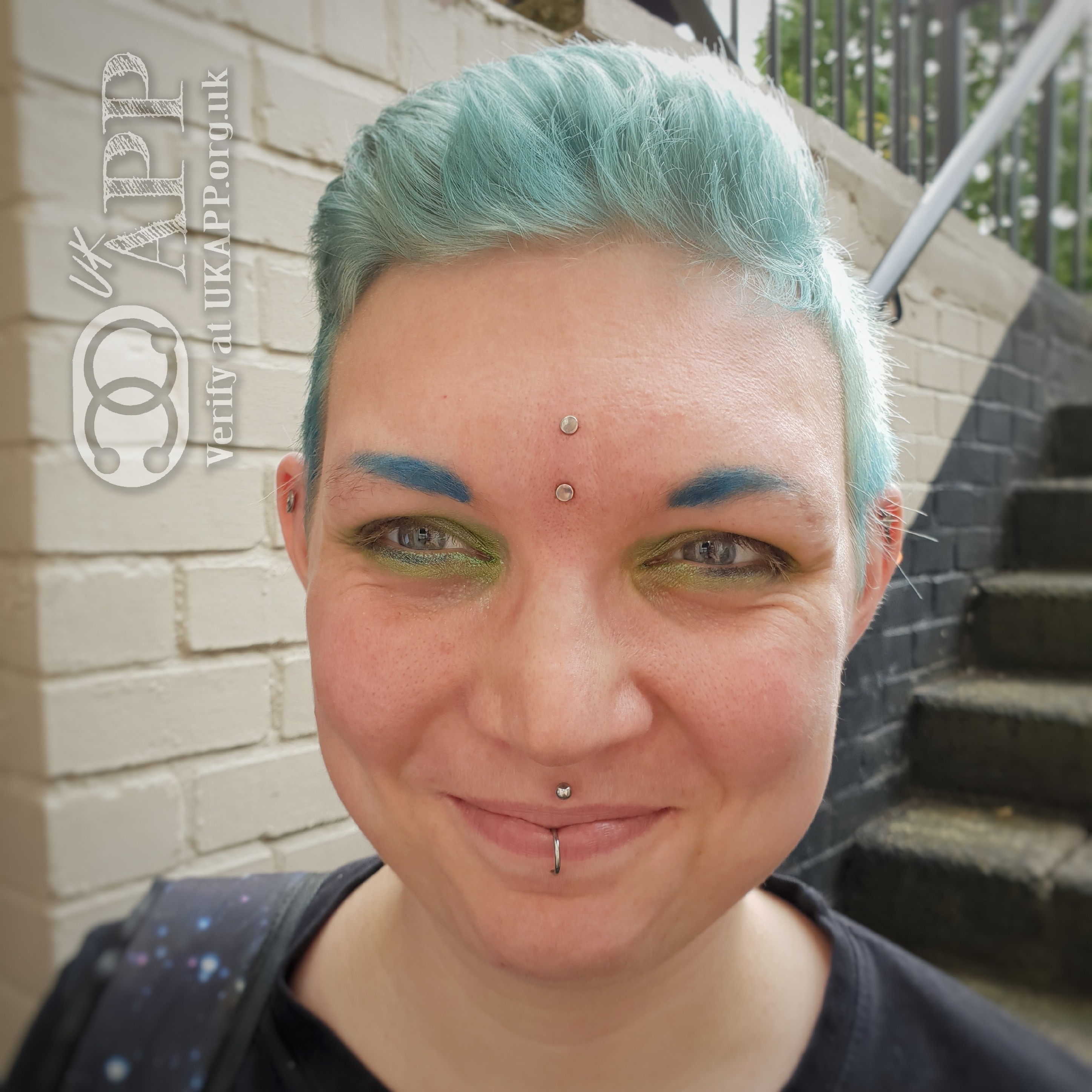 A blue haired Jovian! showing their face with multiple piercings. A vertical surface piercing, medusa and middle lip